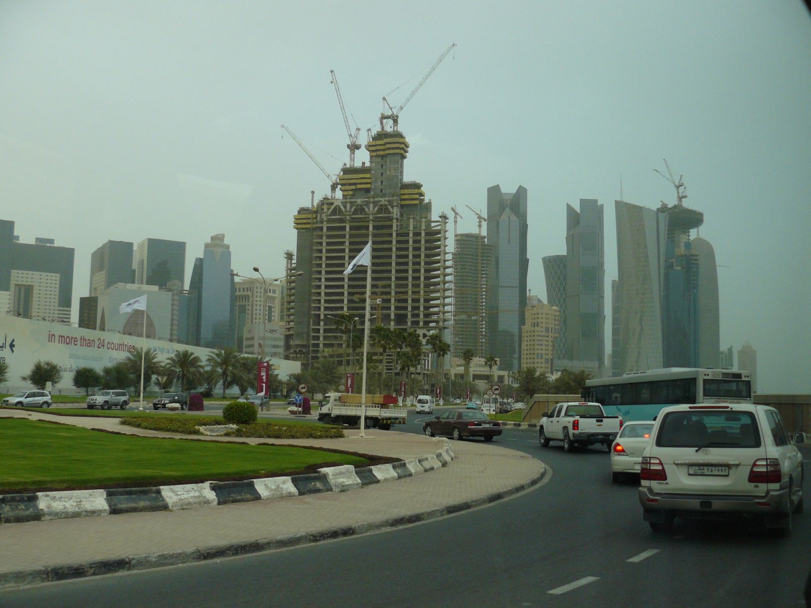 Jellegzetes dohai városkép kész és félkész felhőkarcolókkal és: igen, kivételesen egy igazi városi busz is ott a körforgalomban
